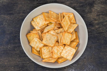 Salty crackers square shape with onion content in bowl on a black surface, top view
