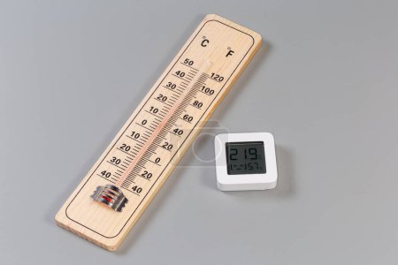 Holzthermometer für Alkohol mit doppelter Skala von Celsius und Fahrenheit und digitales Mini-Thermometer mit Luftfeuchtigkeitsmesser auf grauem Hintergrund