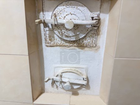 Foto de Puerta de carga de combustible principal de hierro fundido antiguo y puerta del molde de ceniza de la estufa de leña de mampostería cubierta de baldosas para calefacción en interiores - Imagen libre de derechos