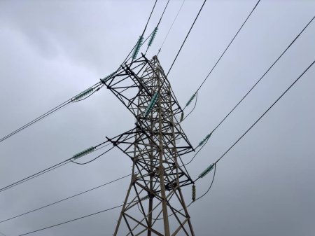 Upper part of steel lattice transmission tower of the overhead power line on a background of cloudy sky, bottom up view