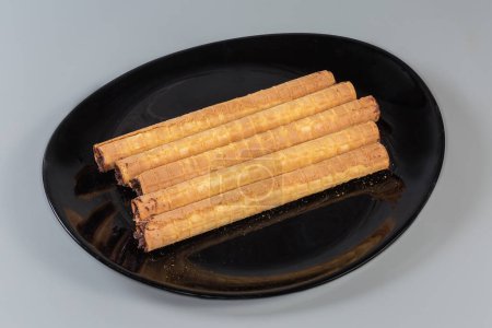 Wafer tubes with filling of chocolate cream on a black dish on a gray background