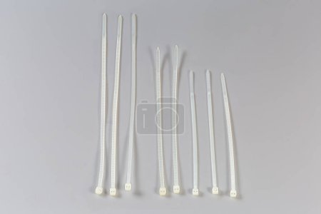 Several unfastened single-use nylon white translucent cable ties of different lengths on a gray background, top view