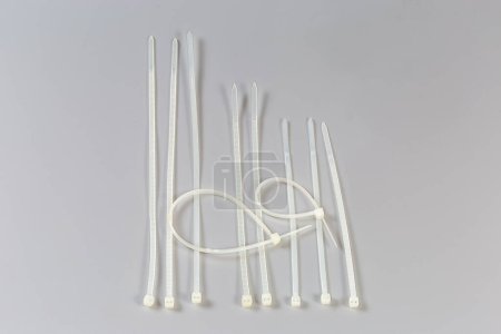 Several unfastened and fastened single-use nylon white translucent cable ties of different lengths on a gray background, top view