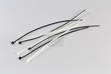 Several black and white unfastened single-use nylon white translucent cable ties on a gray background