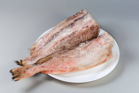 Frozen carcasses of the red cod without heads, covered with hoarfrost on white dish on a gray background
