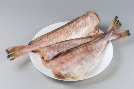 Gekühlte Kadaver vom Kabeljau ohne Kopf, von Fischschuppen befreit auf weißem Teller auf grauem Hintergrund