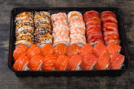 Set der verschiedenen Sushi in offener schwarzer Plastikverpackung zum Mitnehmen auf schwarzer Oberfläche