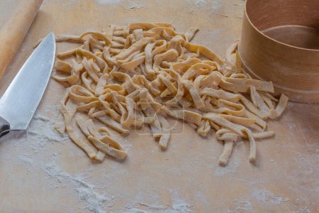 Heap of the raw freshly prepared homemade egg noodles in the shape of the long strips on a wooden board sprinkled with flour