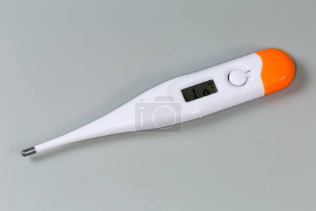 Electronic clinical thermometer with LCD display ready to measure lies on a gray surface, close-up