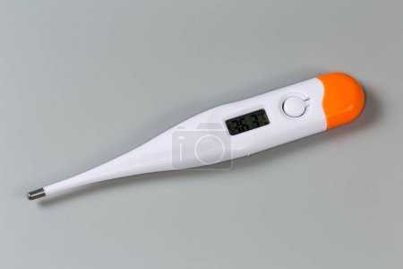 Electronic clinical thermometer with LCD display turned on lies on a gray surface, close-up