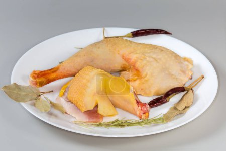 Raw leg and shoulder of rooster grown on the farm by free range method outdoors with yellow skin among the different dry spices on dish on a gray background, side view close-up
