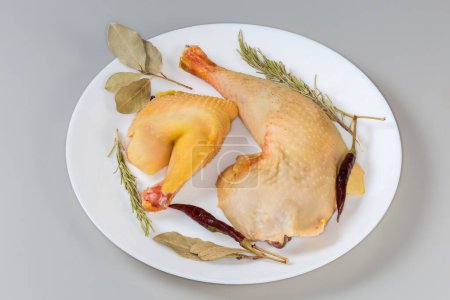 Rohe Hahnenkeule und Hahnenschulter, die im Freilandbetrieb angebaut werden, mit gelber Haut zwischen den verschiedenen trockenen Gewürzen auf einem Teller auf grauem Hintergrund