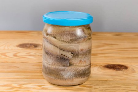 Pickled herring fillets without skin in cooking oil in sealed glass jar on a rustic table, side view
