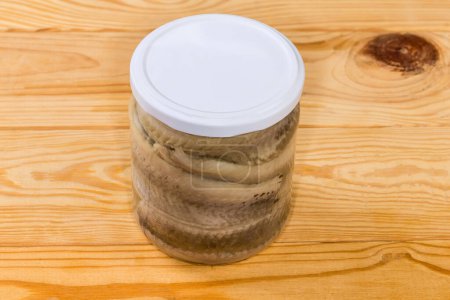 Pickled herring fillets without skin in cooking oil in sealed glass jar on a rustic table, top view
