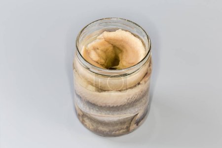 Téléchargez les photos : Filets de hareng marinés sans peau dans de l'huile de cuisson dans un bocal en verre ouvert sur fond gris - en image libre de droit