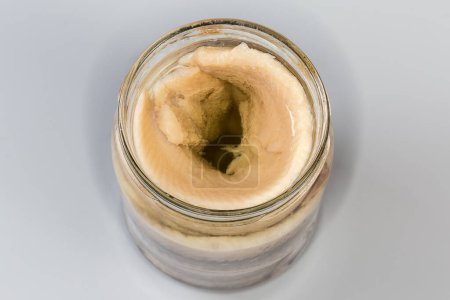 Filetes de arenque en escabeche sin piel en aceite de cocina en frasco de vidrio abierto sobre un fondo gris, vista superior en enfoque selectivo