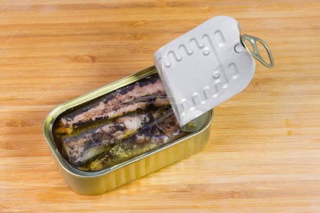 Sardinas enlatadas en aceite de cocina en lata pequeña parcialmente abierta con tapa de lengüeta de anillo-tirón en una superficie de madera
