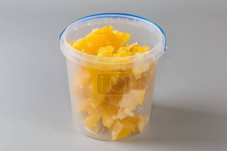 Pieces of crystallized white honey in open round transparent plastic container on a gray background