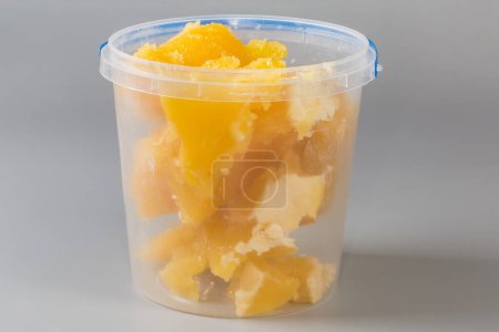 Pieces of crystallized white honey in open round transparent plastic container on a gray background, side view