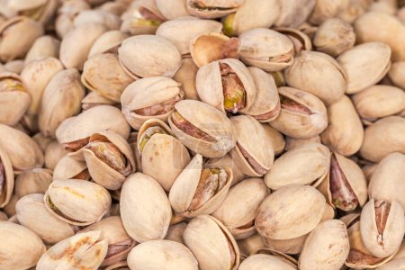 Background of pile of the roasted salted pistachio nuts with naturally partly open shells, top view close-up in selective focus