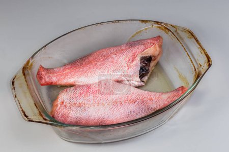 Two raw gutted redfish without heads, also known as ocean perch prepared for baking in the old glass baking dish on a gray background