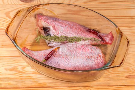 Two raw gutted redfish without heads, also known as ocean perch prepared for baking with dry spices in the old glass baking dish on a rustic table