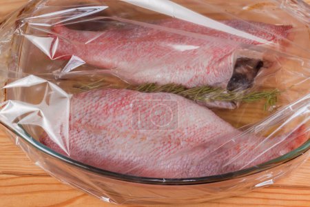 Raw ocean perches without heads prepared for baking in the old glass baking dish placed in the plastic heatproof oven bag, close-up