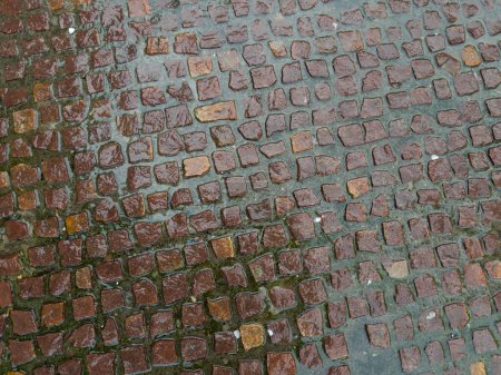 Fragment of footpath paved with small rectangular rubble red stone tiles covered with the water layer during the strong rain, top view