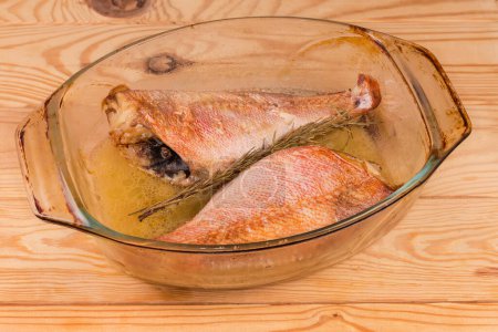 Two baked red fishes without heads, also known as ocean perch in the old glass baking dish on a rustic table