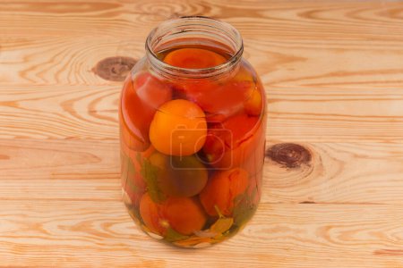 Tomates en conserve de différentes variétés avec des épices et des légumes dans le grand pot en verre ouvert sur une table rustique