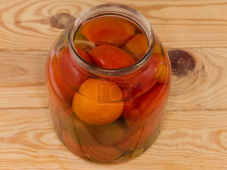 Tomates en conserve de différentes variétés avec des épices et des légumes dans le grand pot en verre ouvert sur une table rustique, vue sur le dessus 