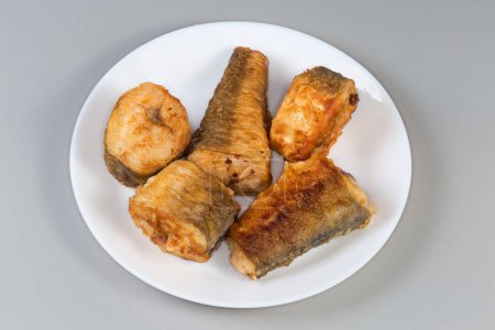 Trozos fritos de merluza hubbsi, o merluza argentina sobre plato blanco sobre fondo gris