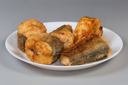 Trozos fritos de merluza hubbsi, o merluza argentina sobre plato blanco sobre fondo gris, vista lateral de cerca