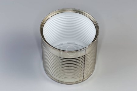 lata vacía abierta de debajo de una comida enlatada, forrada con película de plástico blanco en el interior sobre un fondo gris