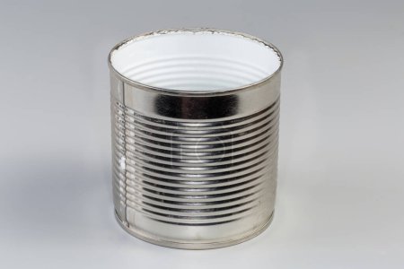 lata vacía de debajo de una comida enlatada, forrada con película de plástico blanco en el interior que se abrió con abrelatas sobre un fondo gris