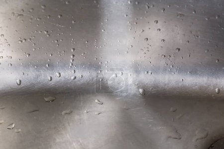Photo for Fragment of the wall and bottom of the old stainless steel kitchen sink covered with water drops, close-up in selective focus - Royalty Free Image