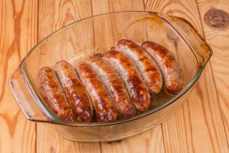 Baked thick pork sausages in natural casing on the old glass casserole pan on a rustic table