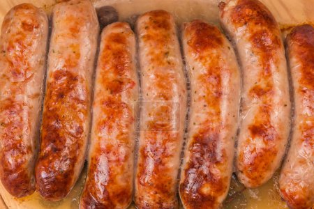 Baked thick pork sausages in natural casing on the old glass casserole pan, fragment close-up top view