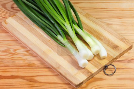 Stems of peeled and washed fresh young green onion on a cutting board on a rustic table
