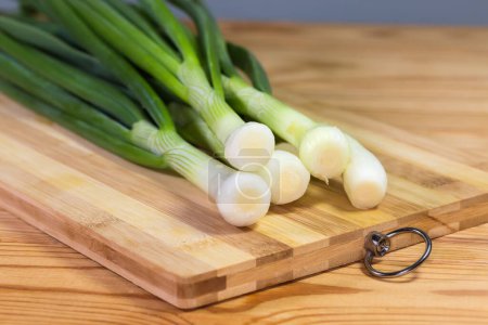 Stems of peeled and washed fresh young green onion on a cutting board on a rustic table, close-up in selective focus