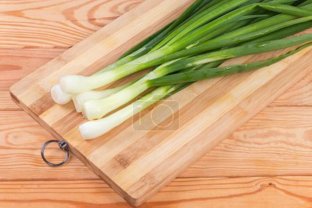 Stems of peeled and washed fresh young green onion on a cutting board on a rustic table