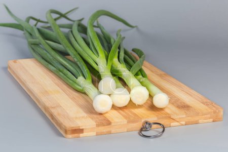 Stems of peeled and washed fresh young green onion on a cutting board on a gray background, close-up in selective focus