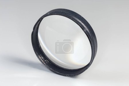 Old simple spherical lens with one convex surface and other flat surface, so-called plano-convex lens in the metal frame on a gray background