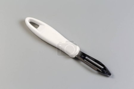 Vegetable peeler with straight fixed blade, so-called French economy straight peeler, and with white plastic handle on a gray background