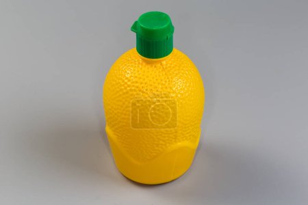 Concentrated lemon juice in yellow plastic container with closed green dosing cap on gray background