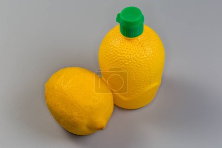 Concentrated lemon juice in yellow plastic container with closed green dosing cap and fresh whole lemon fruit on gray background