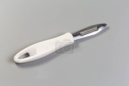 Vegetable peeler with straight fixed blade, so-called French economy straight peeler, and with white plastic handle on a gray background