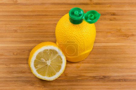 Concentrated lemon juice in yellow plastic container with open green dosing cap and half of fresh lemon on a wooden surface