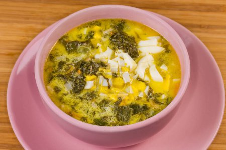 Servir la sopa de acedera, también conocido como borscht verde con huevo duro picado y crema agria en un tazón de color rosa en una mesa de madera, primer plano