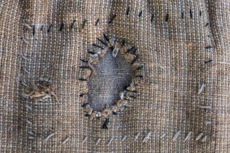 Fragment of the old sack of coarse sackcloth with patch roughly sewn from within with thick black and white threads and covering a torn hole close-up, background, texture